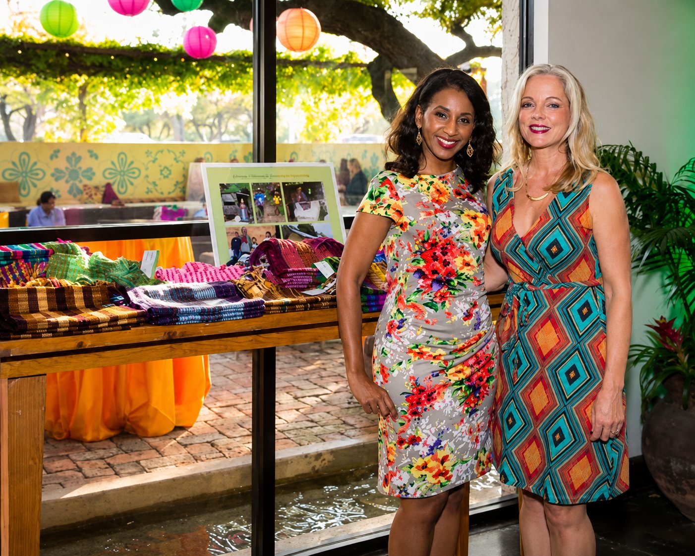 Two guests beside a display of handwoven Guatemalan textiles at a community benefit at Manuel's