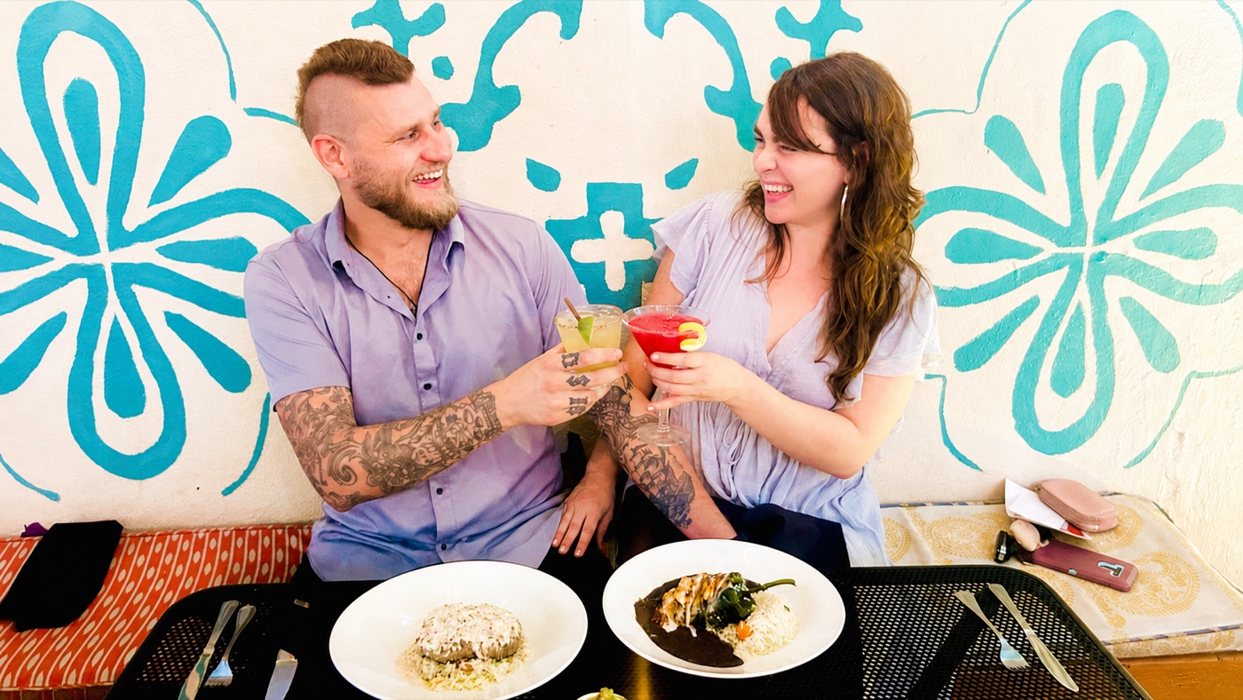 A couple toasting margaritas over their dishes against Manuel's hand-painted talavera patio wall