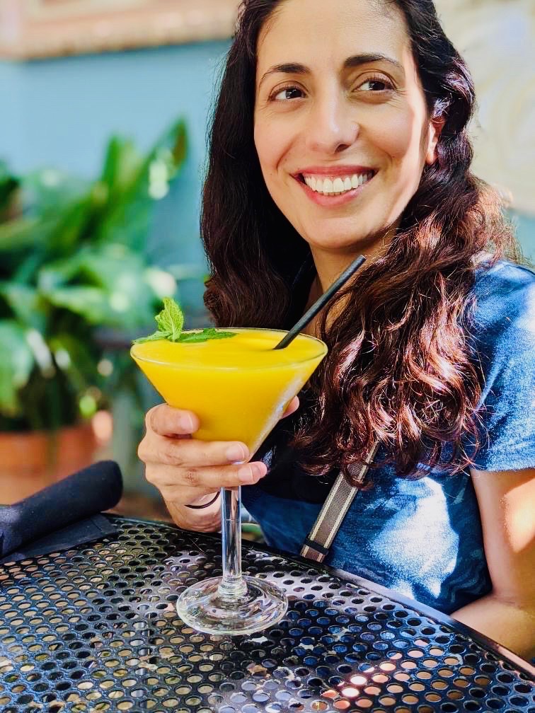 A guest on the patio smiling over a frozen mango margarita garnished with fresh mint at Manuel's