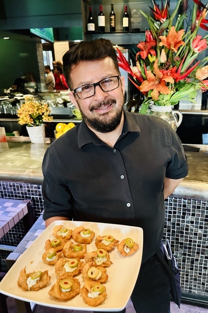 A Manuel's server presenting a plate of appetizers at the bar