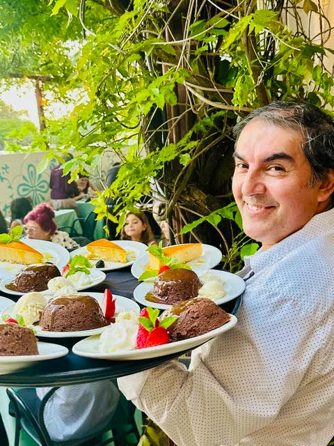 A server carrying a tray of Manuel's desserts — chocolate lava cakes, flan and strawberries — on the shaded patio