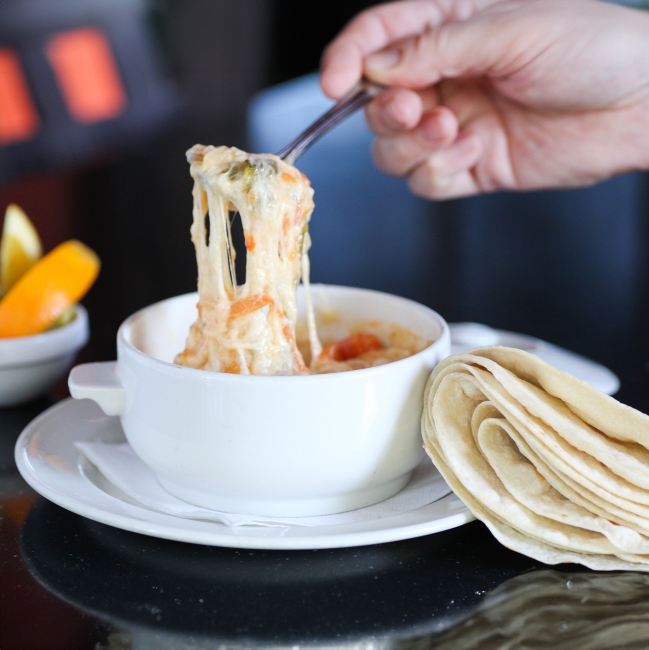Chile con queso pulled from the bowl in a melty cheese stretch, with warm flour tortillas alongside
