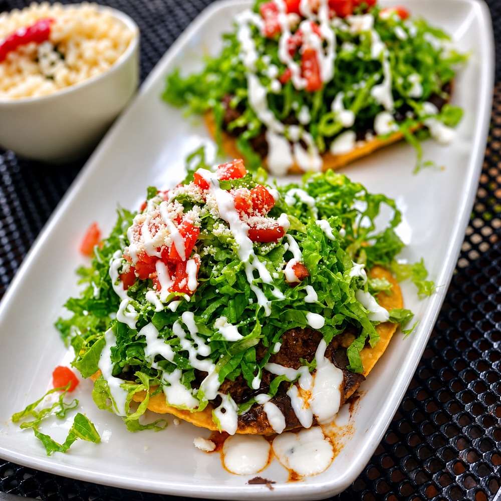 Tostadas Capitalinas — crisp tostadas layered with beans, lettuce, tomato, crema and cotija at Manuel's